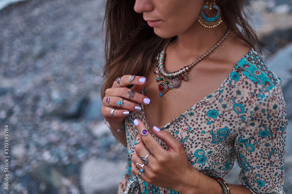 Woman wearing layered boho necklaces and colourful rings, styled with a floral beach dress