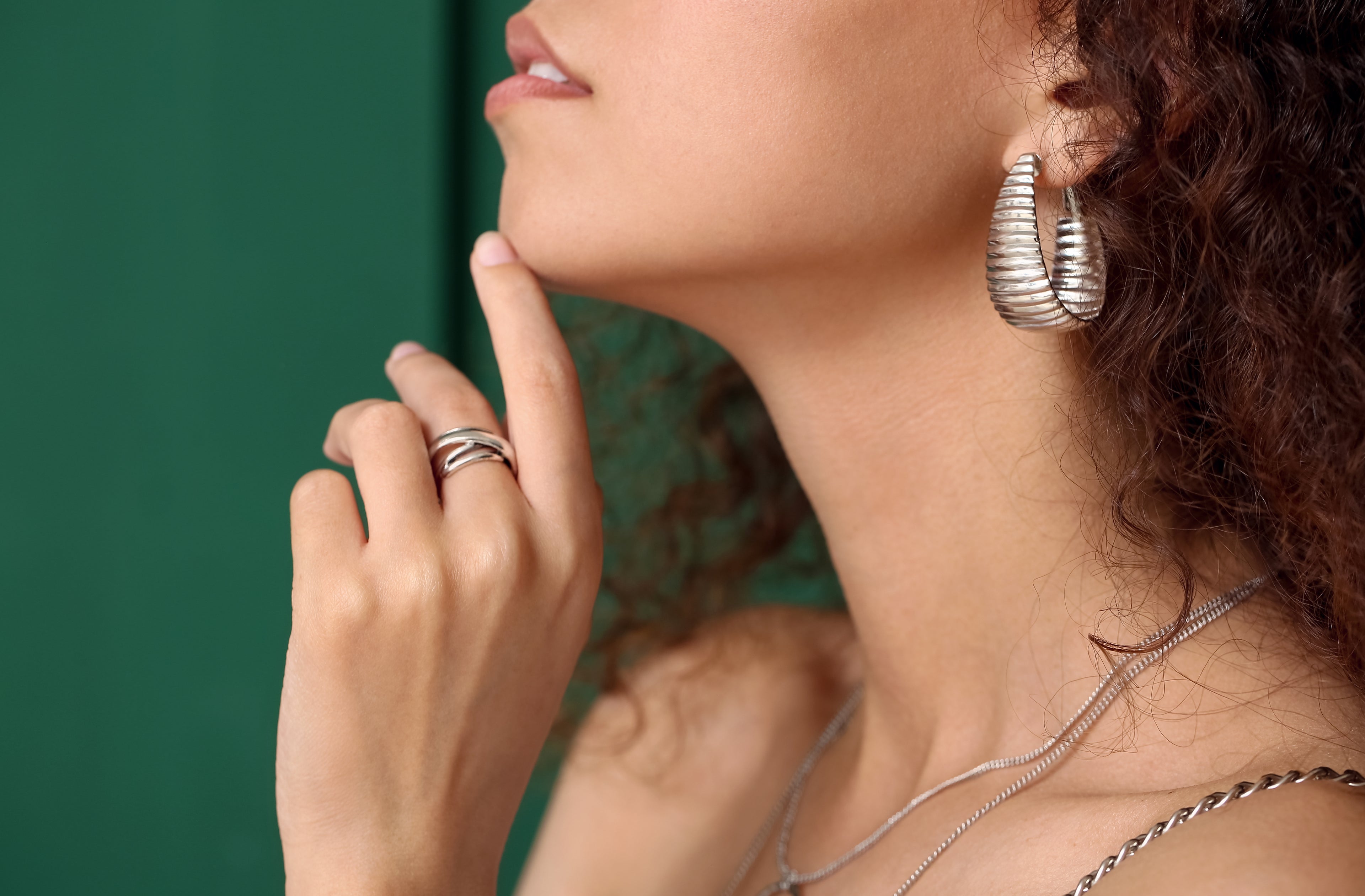 Modern silver jewellery set with bold earrings, layered necklaces, and a statement ring worn by a stylish woman.