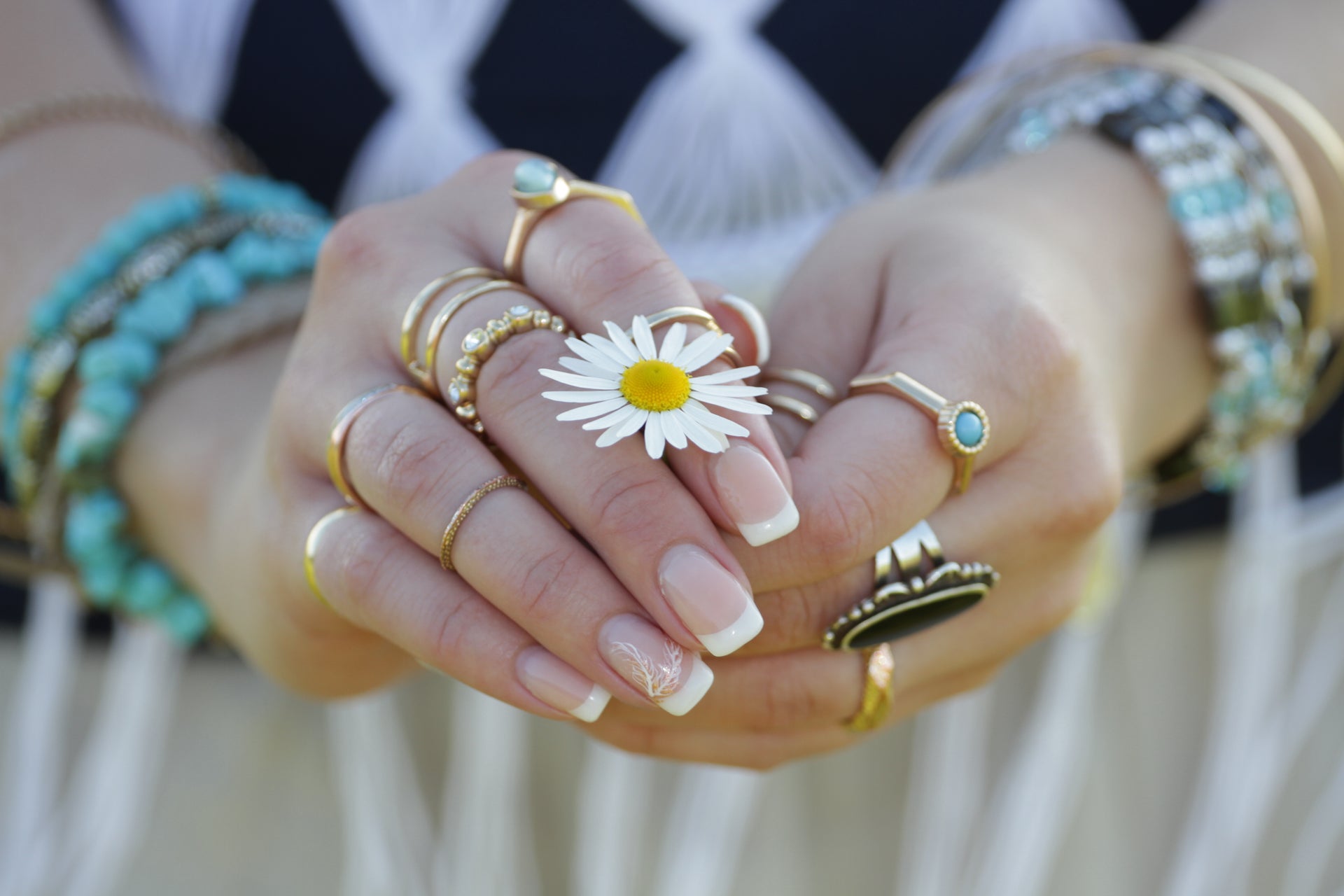 Hand with boho-style stacked rings and bracelets made from recycled materials, holding a daisy for a playful summer vibe