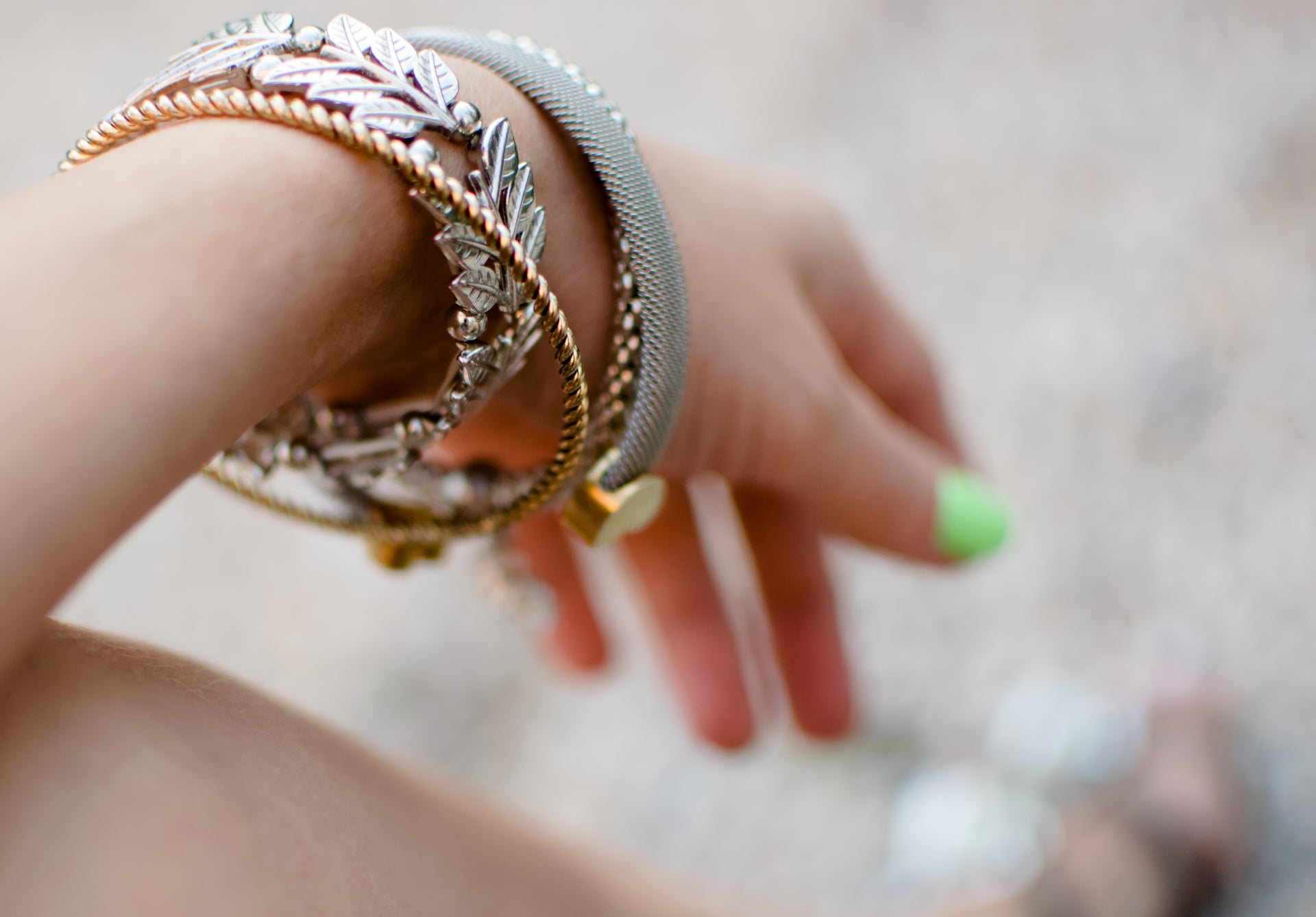 Close-up of a woman's wrist adorned with layered recycled metal bracelets, featuring leaf motifs and textured details