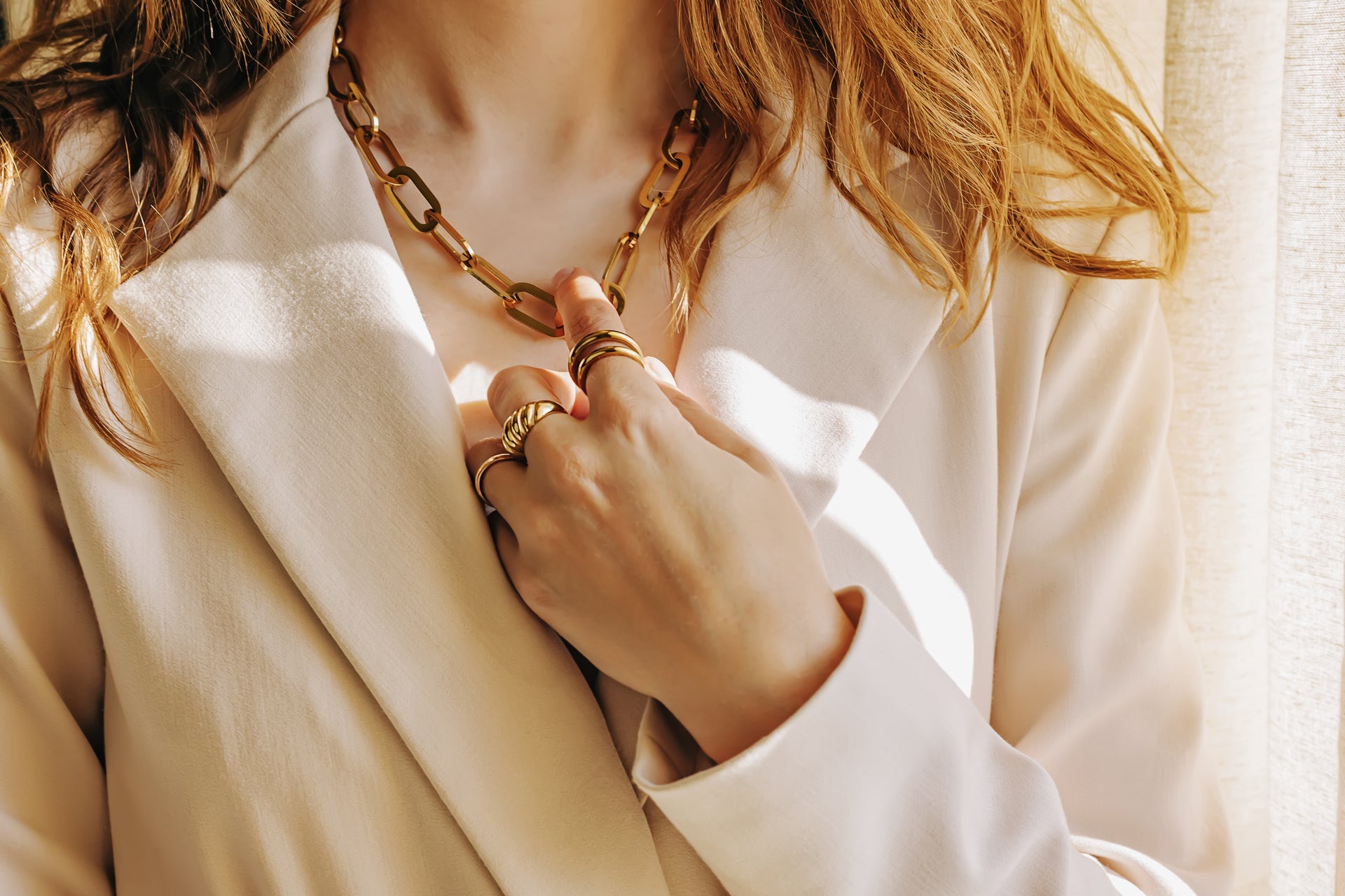 Woman wearing a chunky recycled brass gold chain necklace with matching rings, styled over a cream blazer